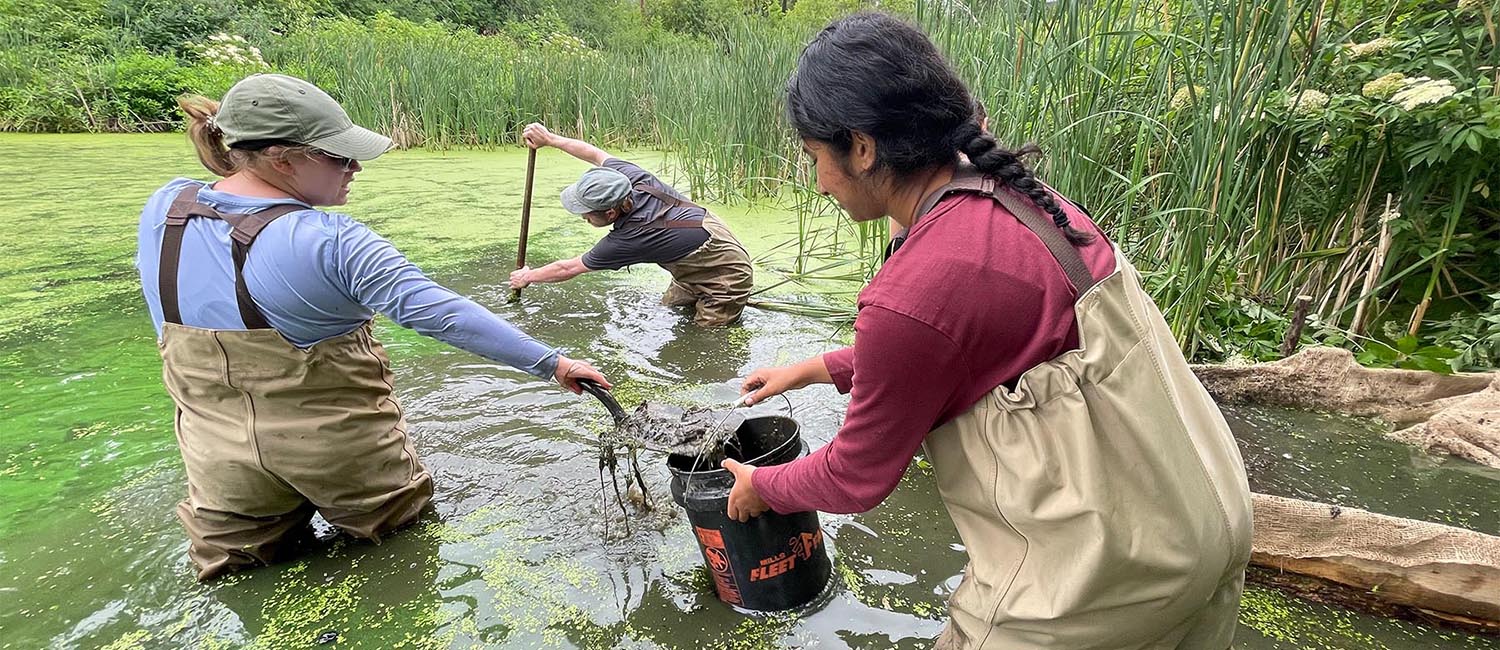 Senior Lecturer Arthur Kneeland (center, back) with LAKES students Evelyn Dyer (left) and Sahi Chundu scooping soil samples from the riverbed.